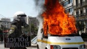 שוטר לצד ניידת שידור עולה באש, יוון (צילום: PIAZZA del POPOLO, רשיון CC BY 2.0)