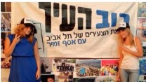 דניאלה סמרי, מגישת החדשות של ערוץ one (מימין), לצד שלט של סיעת רוב-העיר (צילום מסך: דף הפייסבוק של סמרי)