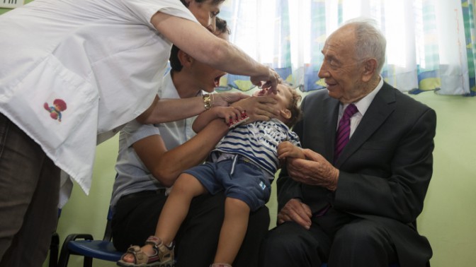 נשיא המדינה שמעון פרס מביט בילד המקבל את החיסון המוחלש נגד פוליו, 21.8.13 (צילום: פלאש 90)