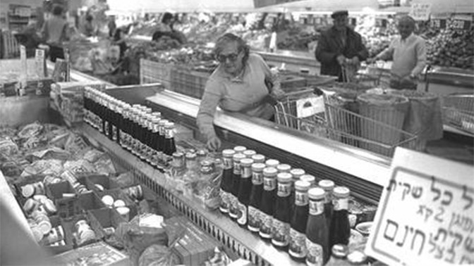 אשה בוחנת מחירי מוצרים בסופרמרקט לאחר יישום "עסקת חבילה א'", שקדמה ל"תוכנית הייצוב". 6.11.1984 (צילום: חנניה הרמן, לע"מ)