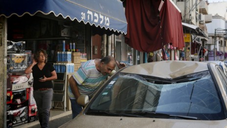ישראלי מביט על רכב שנפגע מרסיס רקטה שיורטה מעל תל-אביב, 10.7.14 (צילום: מרים אלסטר)