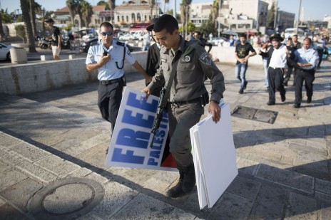 שוטרים מחרימים שלטים בהפגנה בירושלים. מאחור: מפגין, איש נטורי-קרתא, נלקח לחקירה. 27.7.14 (צילום: יונתן זינדל)