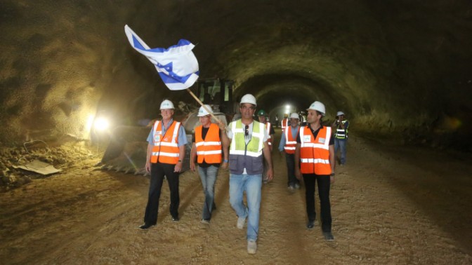 עובדי חברת הדרכים הלאומית מניפים דגל ישראל כשהם צועדים בתוך מנהרה שנחפרה בקו הרכבת המהירה בין תל-אביב לירושלים, 24.7.14 (צילום: יוסי זמיר)