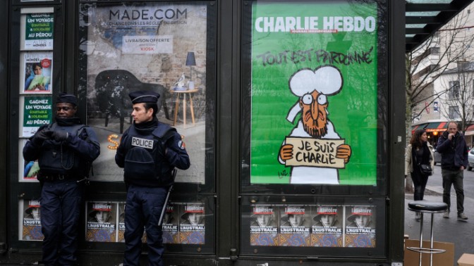 שוטרים עומדים לצד כרזה המציגה את עמוד השער של גיליון המגזין "שרלי הבדו" הראשון שיצא לאחר פיגוע הטרור במערכת העיתון, פריז, 15.1.15 (צילום: סרג' אטאל)
