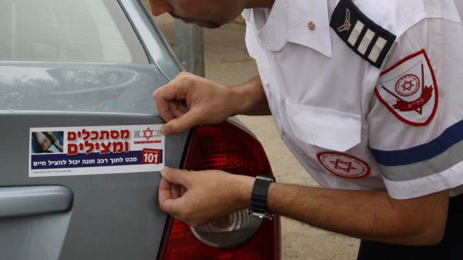 "מסתכלים ומצילים". איש מגן-דוד אדום מדביק סטיקר על מכונית, 2013 (צילום: גרשון אלינסון)