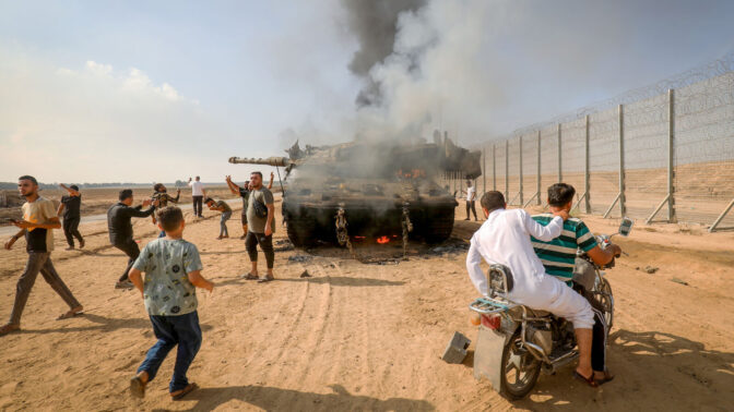 פלסטינים מצטלמים עם טנק צה"לי בוער ב-7 באוקטובר, סמוך לגדר הגבול עם רצועת עזה (צילום: עבד רחים כתיב)