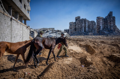 חיילים ישראלים מוליכים צמד סוסים באזור מחנה הפליטים א-שאטי בצפון רצועת עזה, על רקע ההריסות. 16.11.2023 (צילום: יונתן זינדל)