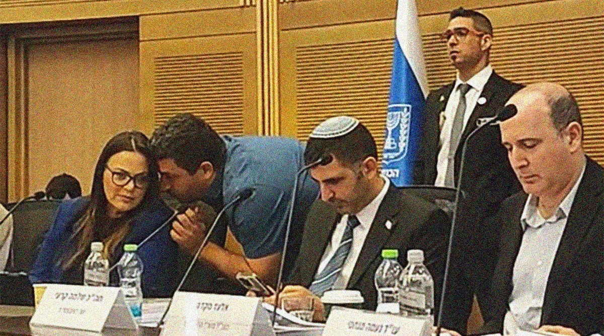 אלעד זמיר, ראש המטה של שר התקשורת שלמה קרעי, לוחש על אוזנה של יו"ר "ועדת התקשורת" ח"כ גלית דיסטל-אטבריאן. מימין: מנכ"ל משרד התקשורת אלעד מקדסי ושר התקשורת שלמה קרעי; ישיבת ועדת התקשורת, 8.12.25 (צילום מתוך שידורי הוועדה)