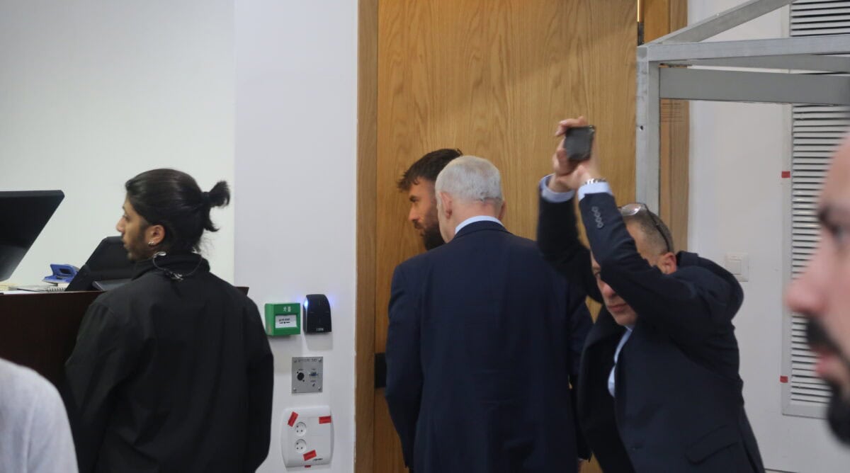 ראש הממשלה הנאשם בשוחד בנימין נתניהו בורח מהצלמים, עם תחילת ההפסקה ביום עדותו ה-79. מניף ידיו כדי להסתירו: דובר הליכוד גיא לוי, 23.2.2026 (צילום: אורן פרסיקו)