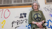 ציפה קמפינסקי על רקע כתובות גרפיטי מהסוג שתיעדה בספרה "הכתובת הייתה". פלורנטין, 18.8.2026 (צילום: איתמר ב"ז)
